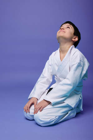 Charming pleasant Caucasian teenage boy in white kimono practicing oriental martial arts, isolated on violet background with copy ad space for textの写真素材