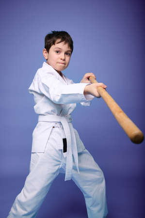 Confident strong concentrated Caucasian teenage boy - Aikido wrestler in white kimono practicing fighting skills with wooden jo weapon in his hands. Oriental martial arts practice concept. Copy spaceの写真素材