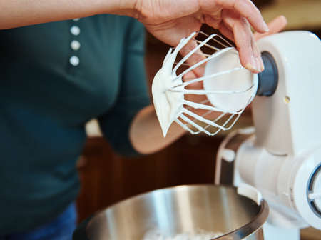 Detail of the chef's hands on the whisk of a food processor with whipped cream. Cooking at home,...