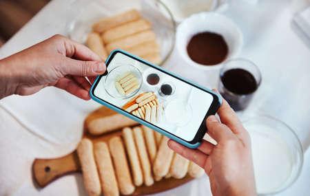 View from above. Hands using smartphone camera and taking photo of ingredients for Tiramisu dessert...