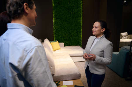 Positive pleasant Hispanic furniture design studio manager working with client in sofa exhibition center. Interior design, human relationships, communication, housing project concept, small businessの写真素材