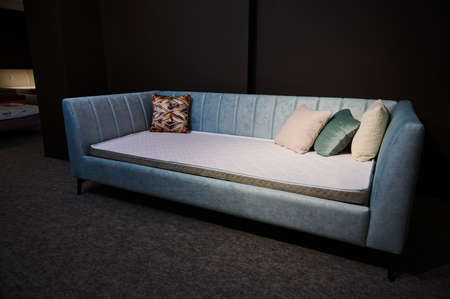 Focus on a turquoise soft velour settee, sofa bed with orthopedic mattress and colorful pastel cushions displayed for sale in a furniture design storeの写真素材