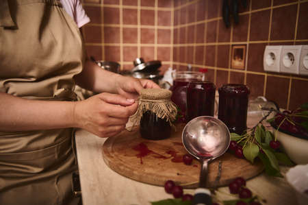 Close-up of the hands of a pastry chef tying a rope on the burlap of the lid of a jar of freshly...