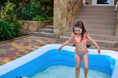 Adorable toddler, baby girl in a bright swimsuit having fun in the inflatable swimming pool in the...