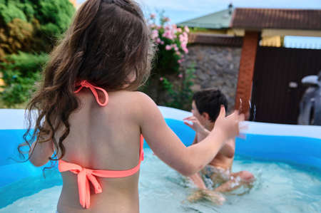 Cheerful Caucasian school age kids, siblings, boy and girl splashing each other with water in the inflatable swimming pool during summer holidays. Happy childhood, summer leisuresの写真素材