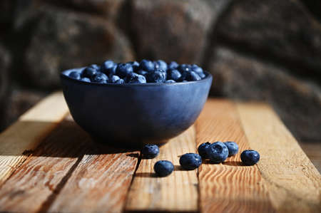 Food composition of a blue ceramic bowl of fresh, ripe and ready-to-eat blueberries on a wooden crate background. Organic farm, healthy eating. Still life. Copy ad space for text. Bannerの写真素材