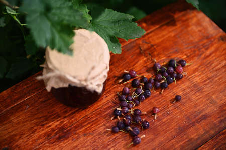 Top view of organic gooseberries scattered on a wooden table and a jar of homemade confiture against...