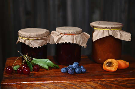 Assortment of homemade confitures of seasonal fruits and berries on rustic wooden background....