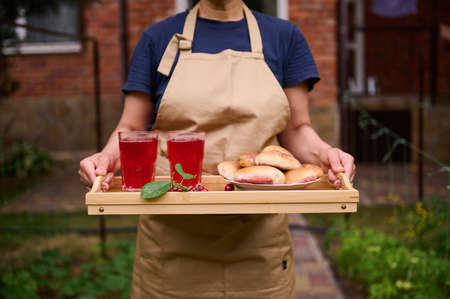 Close-up housewife wearing a chef apron holding a serving tray with freshly baked cherry pies and...