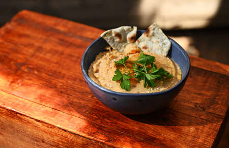 Chickpea hummus dip with pita bread on a blue ceramic bowl, above view on wooden background with...