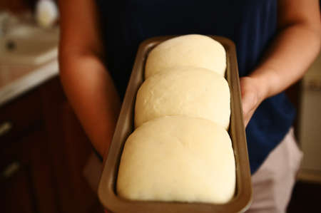 Housewifes hands holding a baking container with suitable yeast dough for bread. Cooking healthy whole grain breadの写真素材