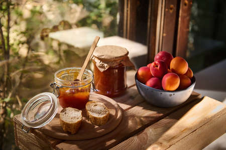 Still life. Homemade jam in jar, slices of freshly baked bread and sweet ripe organic apricots against a wooden windowの写真素材