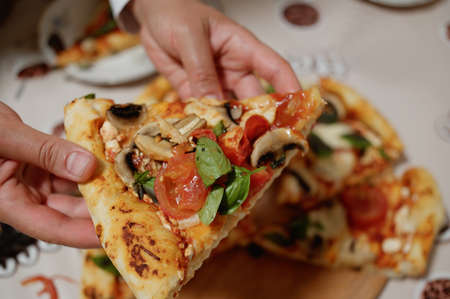 Selective focus, woman hands holding a slice of delicious appetizing homemade freshly baked Italian pizza with organic juicy tomatoes, mushroom champignons, mozzarella cheese and fragrant basil leavesの写真素材