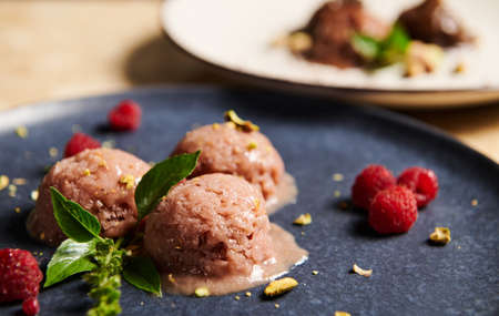 Close-up. Scoops of raspberry ice cream, sorbet with sprinkled pistachio, raspberries and lemon basil on dark blue plate. Healthy raw vegan, refreshing dessert. Summer food still life. Selective focusの写真素材