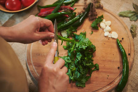 Top view of the hands of a housewife chopping fresh fragrant culinary herbs on a wooden cutting board while preparing a pickle marinade for pickling chili peppers in the home kitchen. homemade foodの写真素材