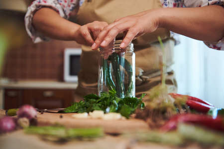 Close-up of filling sterilized glass jar with spicy chili peppers, chopped fresh dill leaves, garlic when pickling seasonal vegetables in the kitchen. Canning food and making preserves for the winter.の写真素材