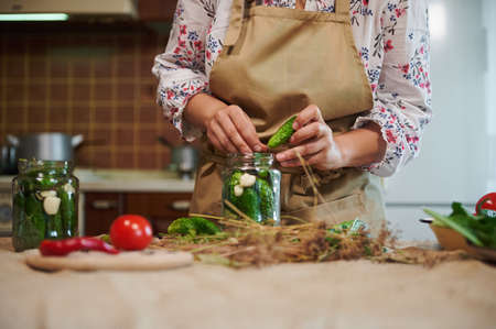 Various fresh vegetables on bowls, prepared for home pickling. Womens hands put cucumbers in a can...