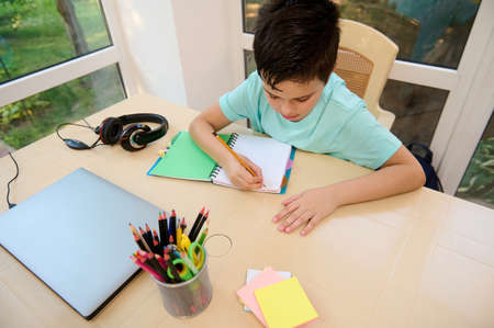 View from above of smart schoolboy writing an essay, doing his homework. Concept of back to school....