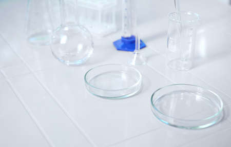 Glass lab dishes on white table on the background of labware such as beaker, flask, graduated cylinders, test tubes. Science chemistry. Scientific biological and chemical laboratory with copy ad spaceの写真素材