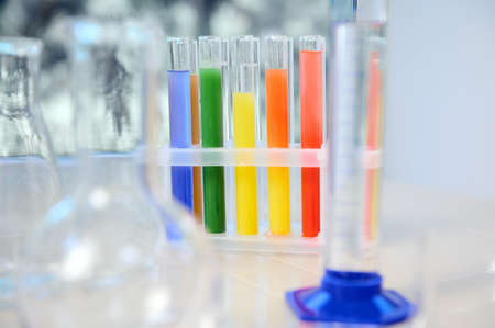 Focus on test tubes with rainbow colored chemicals and reagents standing on tripod. Blurred foreground with graduated cylinder, flasks and measuring glass labware. Chemistry, science conceptの写真素材