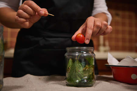 Details: Chefs hands putting fresh organic home grown cherry tomato in sterilized jar, while canning delicacy for organic seasonal vegetables for winter. Preserving food. Pickling. Marinating.の写真素材