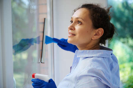 Close-up of multi-ethnic pretty woman, maid, housewife, homemaker spraying detergent and removing...
