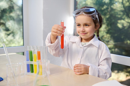 Pretty child chemist, scientist, Caucasian preschooler little girl wearing safety goggles and lab coat doing chemistry experiments, watching the fascinating chemical reaction in the test tube.の写真素材