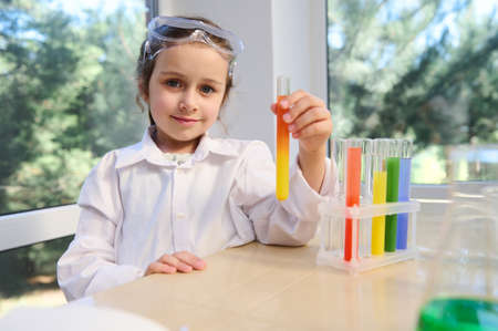Adorable little girl, future scientist chemist fascinated by leaning chemistry, standing at table with tripod and test tubes with going chemical reactions. Learning new science. Miracles of Chemistryの写真素材