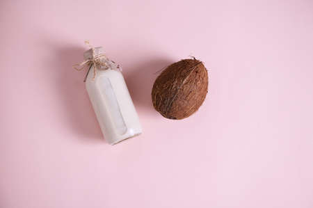 Flat lay composition with a bottle of a raw vegan, healthy organic plant based milk and a coconut, palm fruit isolated over pink background with copy space for advertising textの写真素材