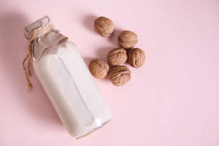 Still life with a plant based milk in a glass bottle, alternative non dairy drink and a heap of organic wholesome walnuts on a pink background with advertising copy space. Healthy food and drinkの写真素材