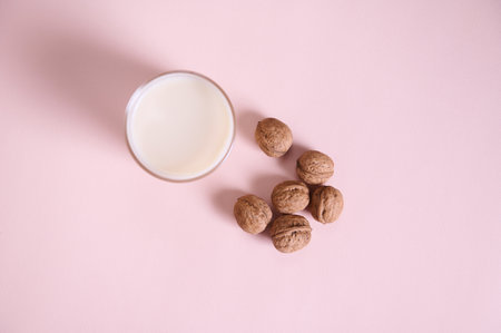 Flat lay with a vegetable milk in a drinking glass, alternative lactose free drink and a handful of organic wholesome walnuts on a pink background with advertising copy space. Healthy food and drinkの写真素材