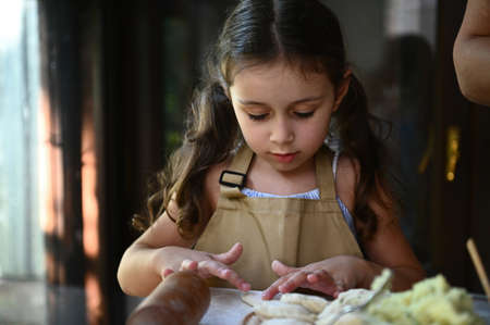 Close-up portrait of charming baby girl with two ponytails, wearing beige chefs apron, molding...