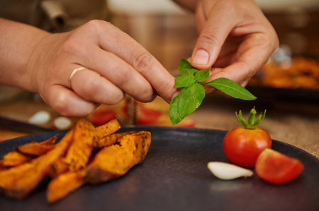 Close-up of serving dish. Selective focus on the hands of a chef putting a basil leaf on the top of...