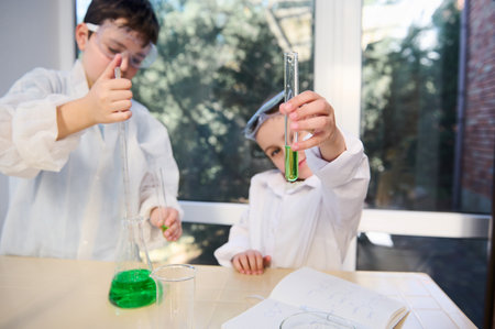 Selective focus on a test tube with green chemical solution in the hands of blurred child girl, watching the going on chemical reaction. Kids learning Chemistry. School laboratory. Knowledge Educationの写真素材