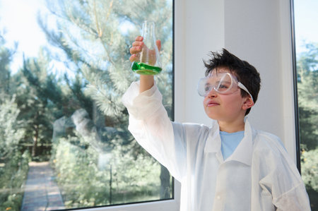 Adorable Caucasian dark-haired child, a smart schoolboy wearing safety goggles and lab coat, examining the chemical reaction going on in the flask. Learning Chemistry on new semester of a school yearの写真素材