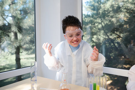 Mischievous teenage boy in safety eyewear and lab coat, fascinated by scientific experiments in chemistry laboratory. Concept of Back to school. Open to new knowledges on of the academic year semesterの写真素材