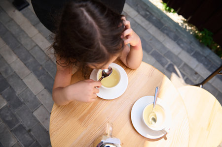 Overhead view of a cute child, drinking healthy herbal drink from a spoon, sitting at a table in the summer terrace. Tea timeの写真素材
