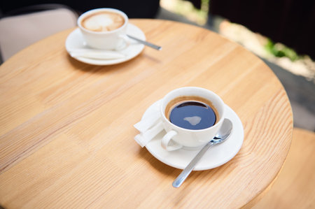 Top view of white cups of aromatic coffee americano and cappuccino on a wooden table, in the summer terrace of a cafeteria. Food and drink. Copy advertising space. Still lifeの写真素材