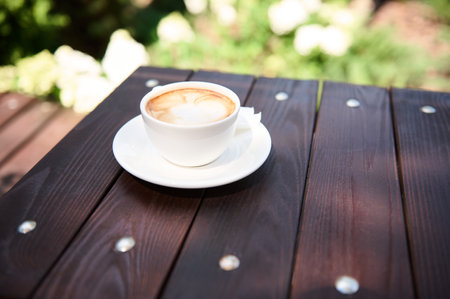 Still life with a white cup of frothy cappuccino with foam on a wooden table, in the summer terrace of a cafeteria. Food and drinkの写真素材