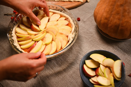 Close-up. Hands of a woman housewife or chef confectioner, putting slices of apple in circle on top of pumpkin pie. Preparing traditional American classic festive pie for Thanksgiving Day. Halloweenの写真素材