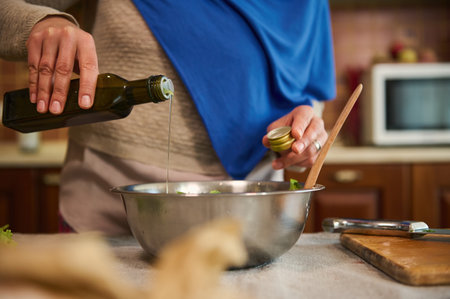 Close-up. Selective focus. Unrecognizable woman, housewife in a blue hijab, pours olive oil into a bowl with fresh healthy raw vegan vegetable salad. Cooking. Cookery. Healthy eating. Vegetarianismの写真素材