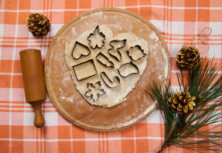 View from above of cookie cutters on the gingerbread dough, rolled out on a wooden board, next to a...