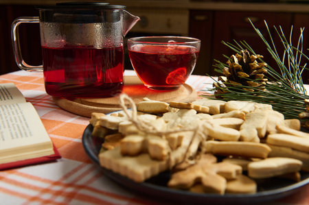 Hot winter drink: Hibiscus tea in a teapot and homemade gingerbread cookies on a plate. Christmas time. Cozy home atmosphere. Fir-tree branch and golden pine cones as decor. Holiday mood in the airの写真素材