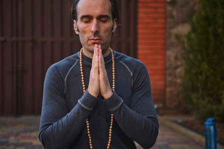 Selective focus on hands of a peaceful relaxed Caucasian man athlete, a yogi, keeping palms together, meditating with closed eyes, doing breathing and body relaxing exercises outdoors. Yoga practiceの写真素材