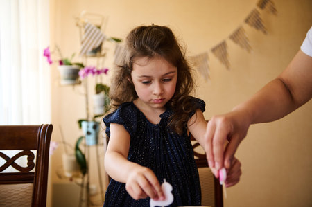 Adorable Caucasian little girl with curly long hair, wearing an elegant navy dress with golden polka...