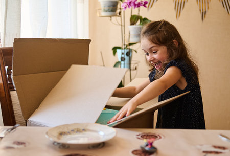 Happy excited little child, a birthday girl, opening a huge gift box and taking out her birthday present, experiencing surprise, excitement, astonishment and happiness. Birthday party. Anniversaryの写真素材