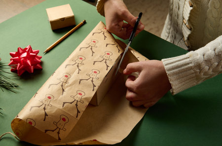 Top view woman packing a present for Christmas or New Year's events, using beautiful decorative wrapping paper with deer pattern, over a green background. Boxing Day. Xmas preparations. Copy ad spaceの写真素材