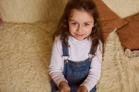 Portrait of a Caucasian cute child, adorable baby girl, sweetly smiling a beautiful toothy smile looking at camera, sitting on a comfy sofa at home interior.の写真素材