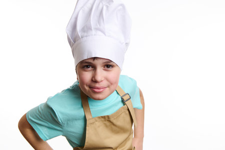 Close-up of an overjoyed happy pre-adolescent child- chef pastry, cook, baker confectioner wearing chef hat and beige apron, isolated on white background. Free ad space. Culinary and bakery conceptの写真素材