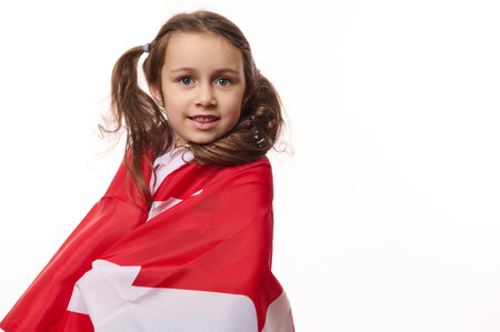 Close-up portrait of American citizen, little child girl wrapping in Canadian flag, isolated on white background. Canada Independence Day. Dominion Day. 1st July. Concept of emigration and citizeshipsの写真素材
